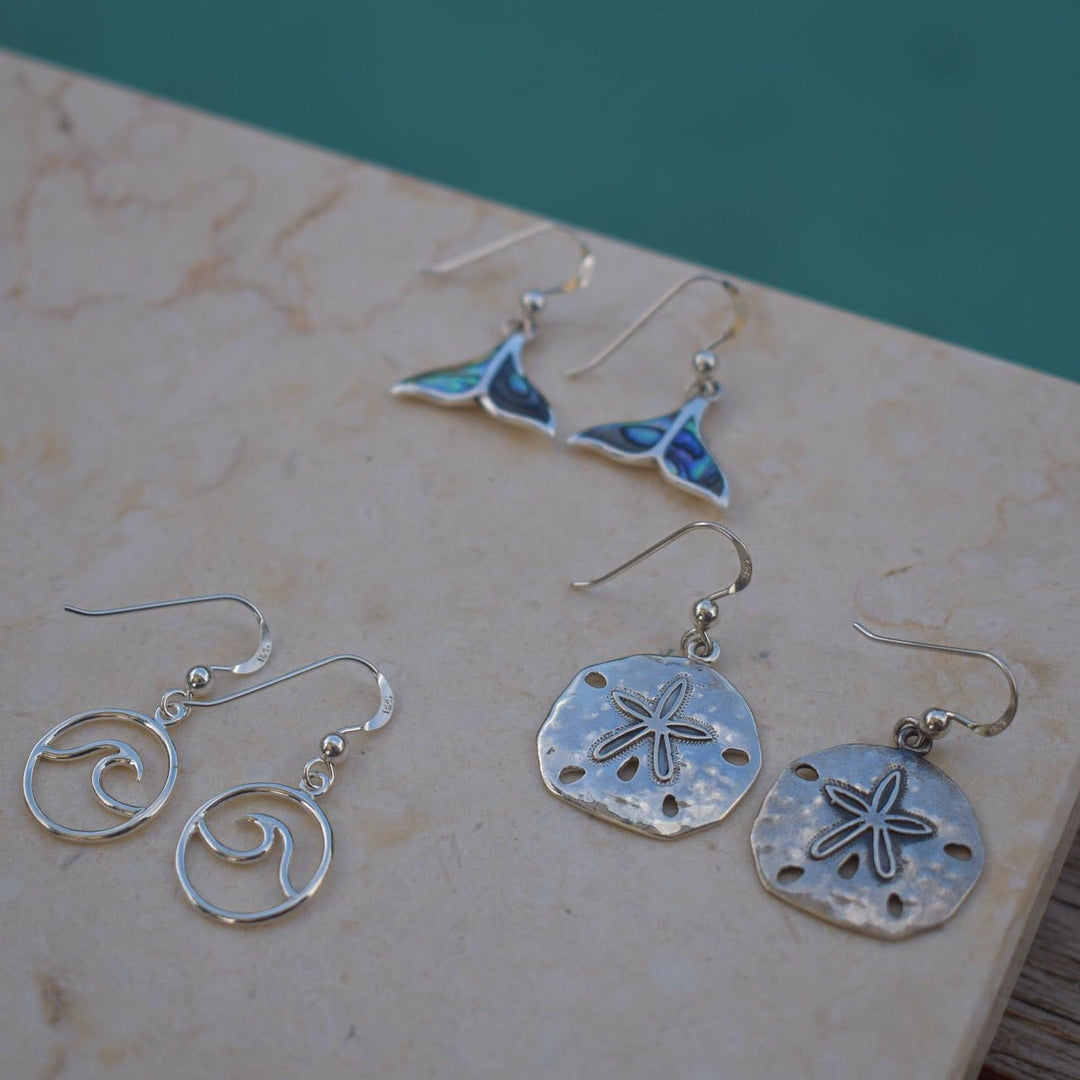 Close-up of abalone shell whale tail earrings in sterling silver on natural display