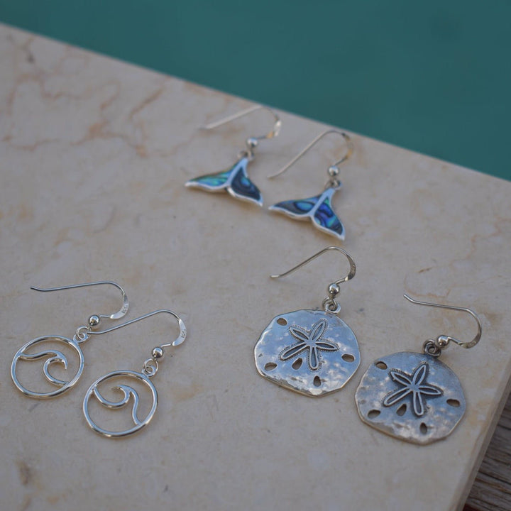 Close-up of abalone shell whale tail earrings in sterling silver on natural display
