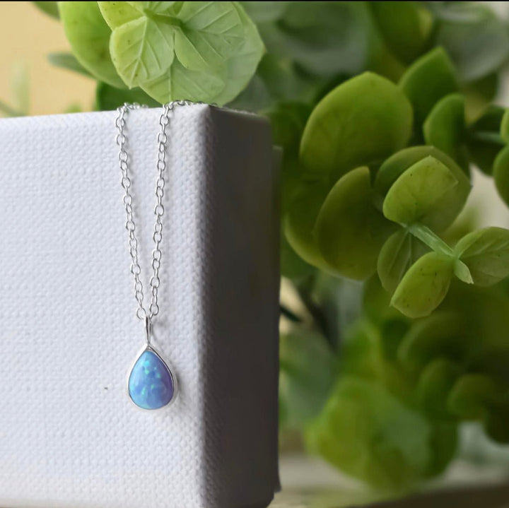 Close-up of lab-grown blue opal pear-shaped necklace in sterling silver on natural display