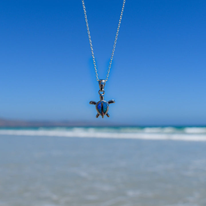 Close-up of sterling silver turtle necklace with blue opal inlay on beach background