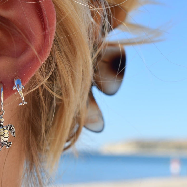 Dolphin stud earrings in sterling silver worn close to the ear, ocean-themed design