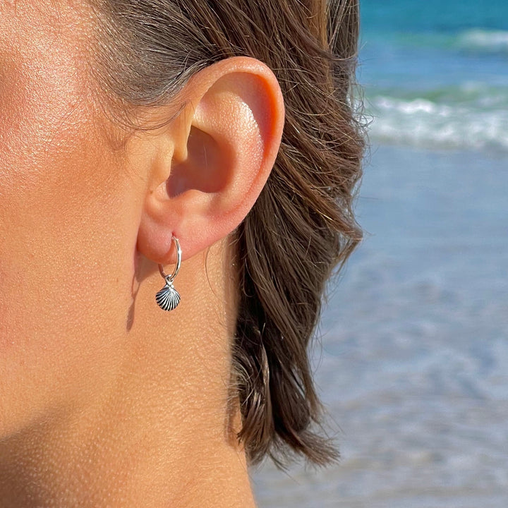 Seashell charm hoop earrings in sterling silver worn on ears, beach-style jewellery