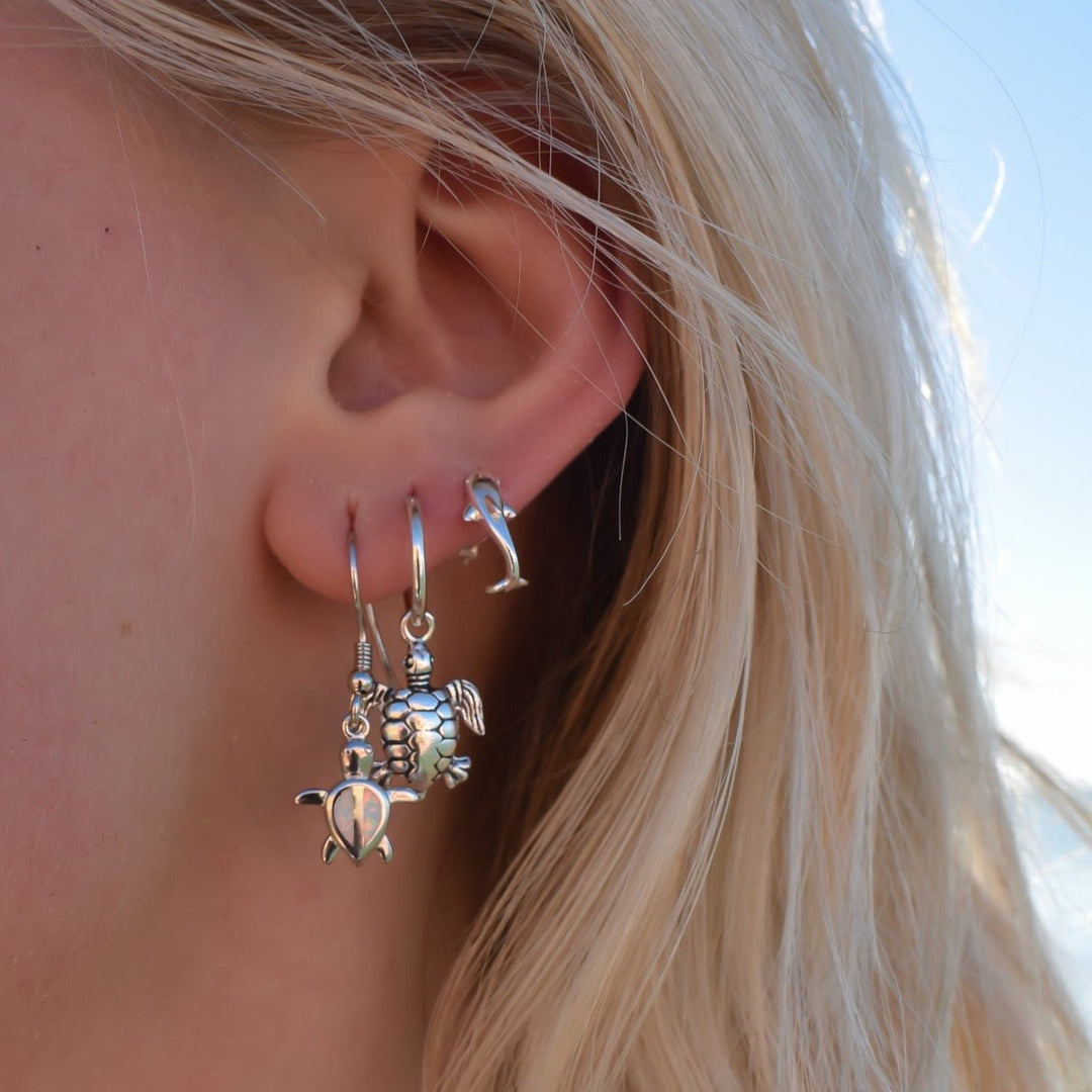 Sterling silver dolphin earrings styled with beachy jewellery, worn from side view