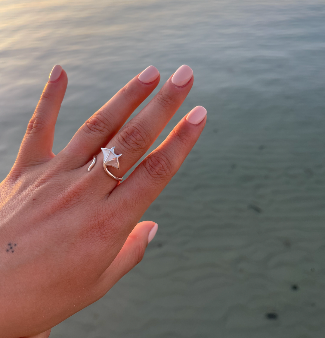 Sterling silver manta ray ring with mother of pearl inlay, photographed in front of a tropical ocean background