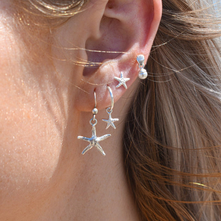 Starfish stud earrings in sterling silver worn on ears, inspired by the sea