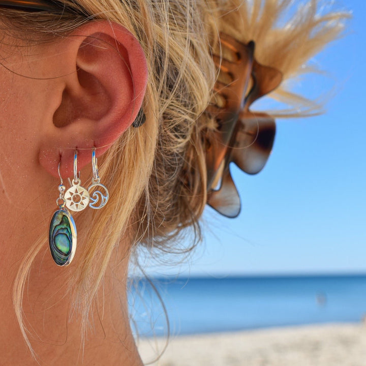 Wave and sun mismatched hoop earrings in sterling silver worn on ears, beach-inspired style