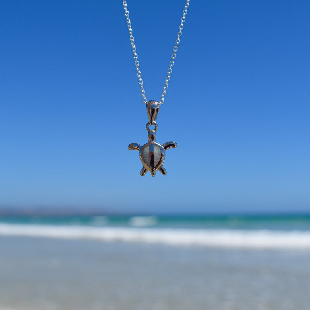 Close-up of white opal turtle necklace in sterling silver at the beach