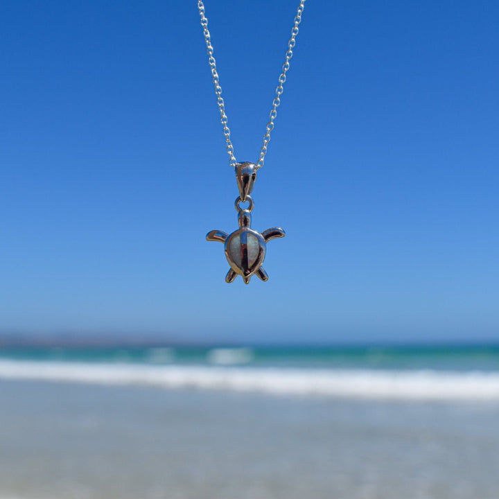 Close-up of white opal turtle necklace in sterling silver at the beach